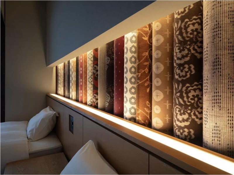 Rouleaux de kasuri de Kurume en tête de lit éclairée, chambre du ryokan Taisenkaku